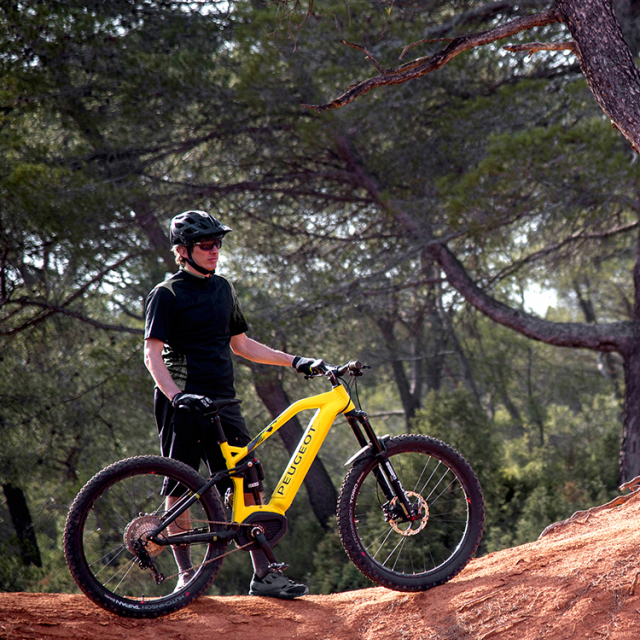 Biker holding his Peugeot integrated battery electric MTB on a mountainous path